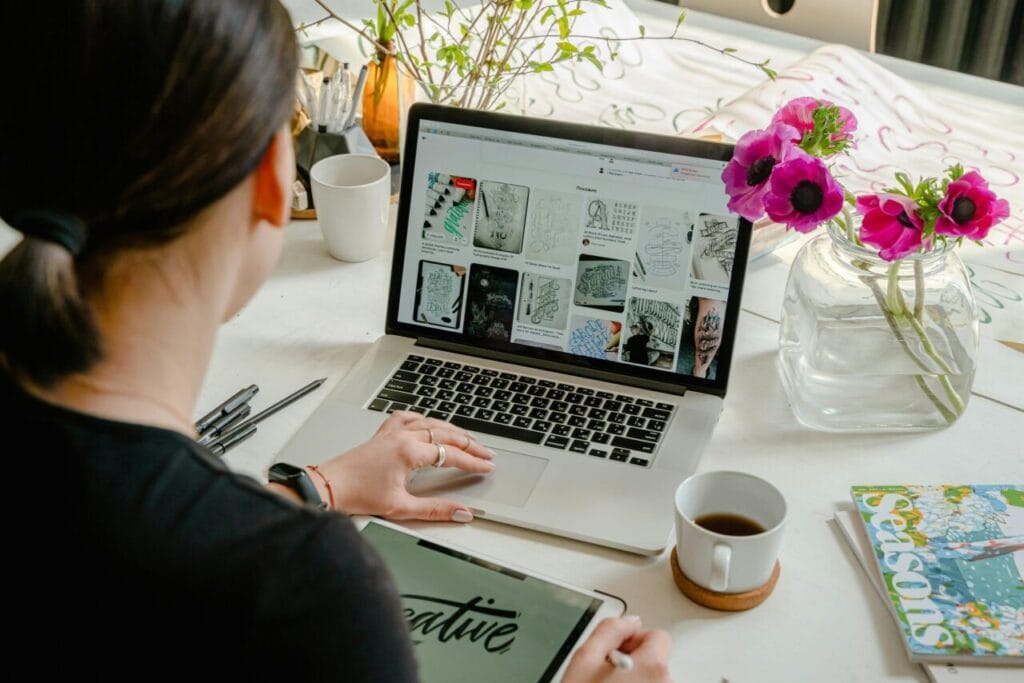 Woman in a creative workspace using a laptop and tablet for calligraphy. Artistic and tech-driven environment.